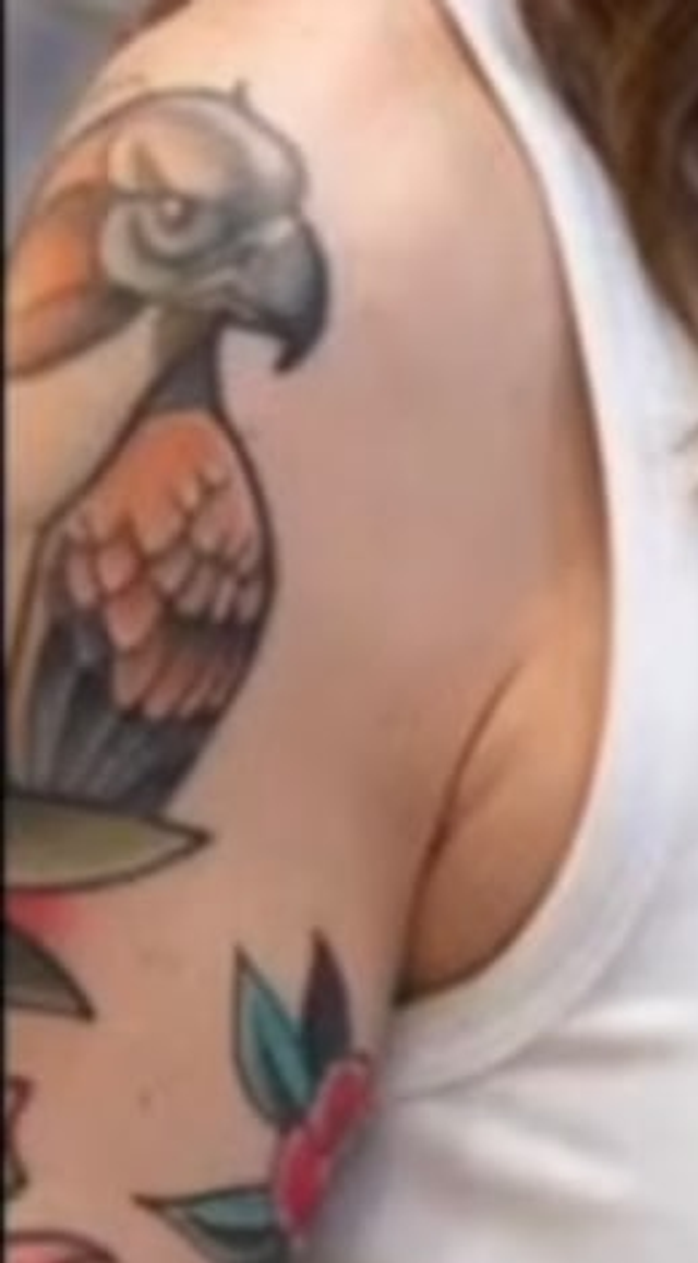 Close-up detail of the tank-top frame: a neo-traditional eagle tattoo in orange and grey on the upper arm, with a red-and-green rose and leaves below the shoulder.