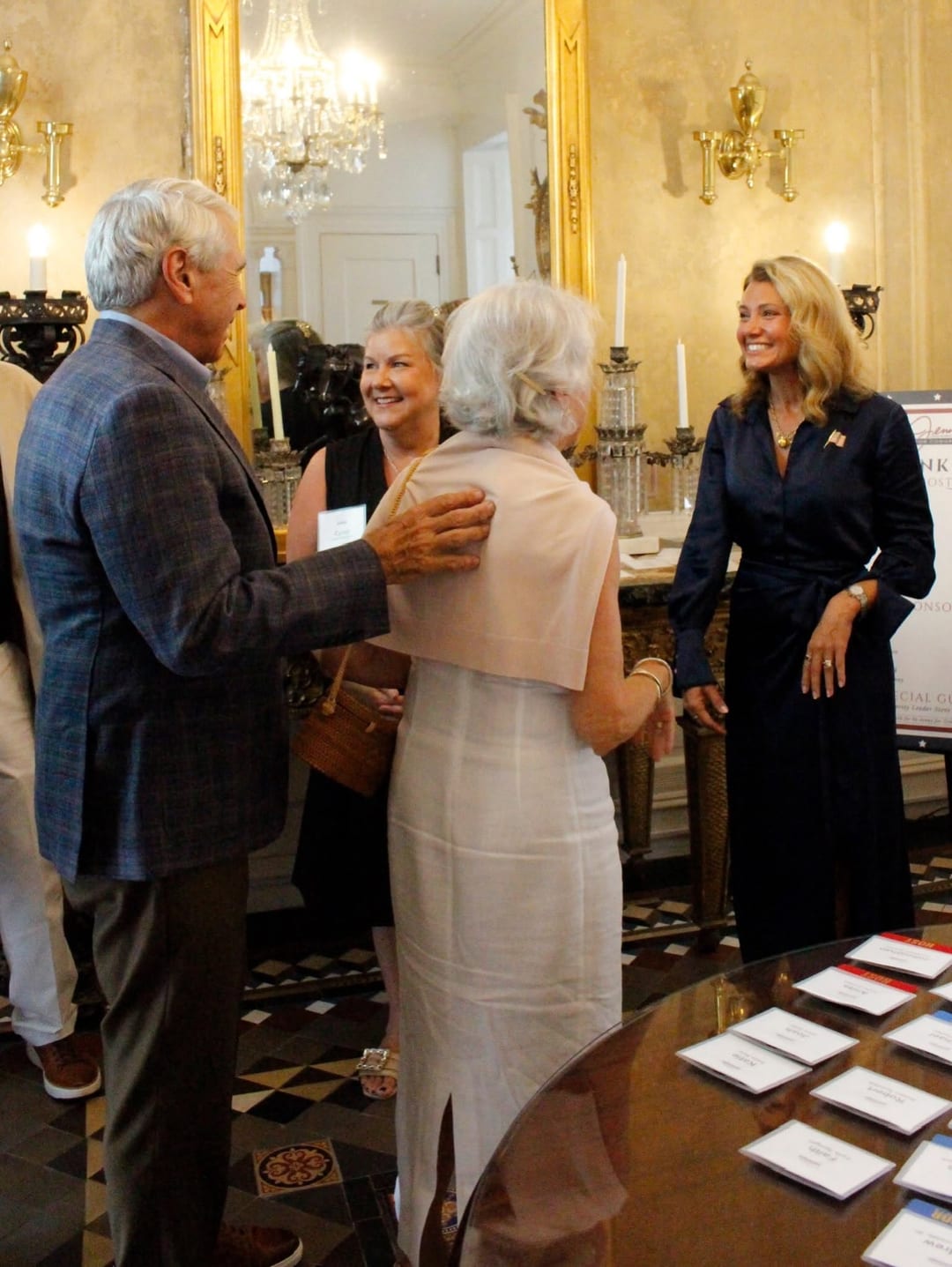 Guests greet one another at Jenny Costa Honeycutt's Charleston reception, with campaign signage visible at right.
