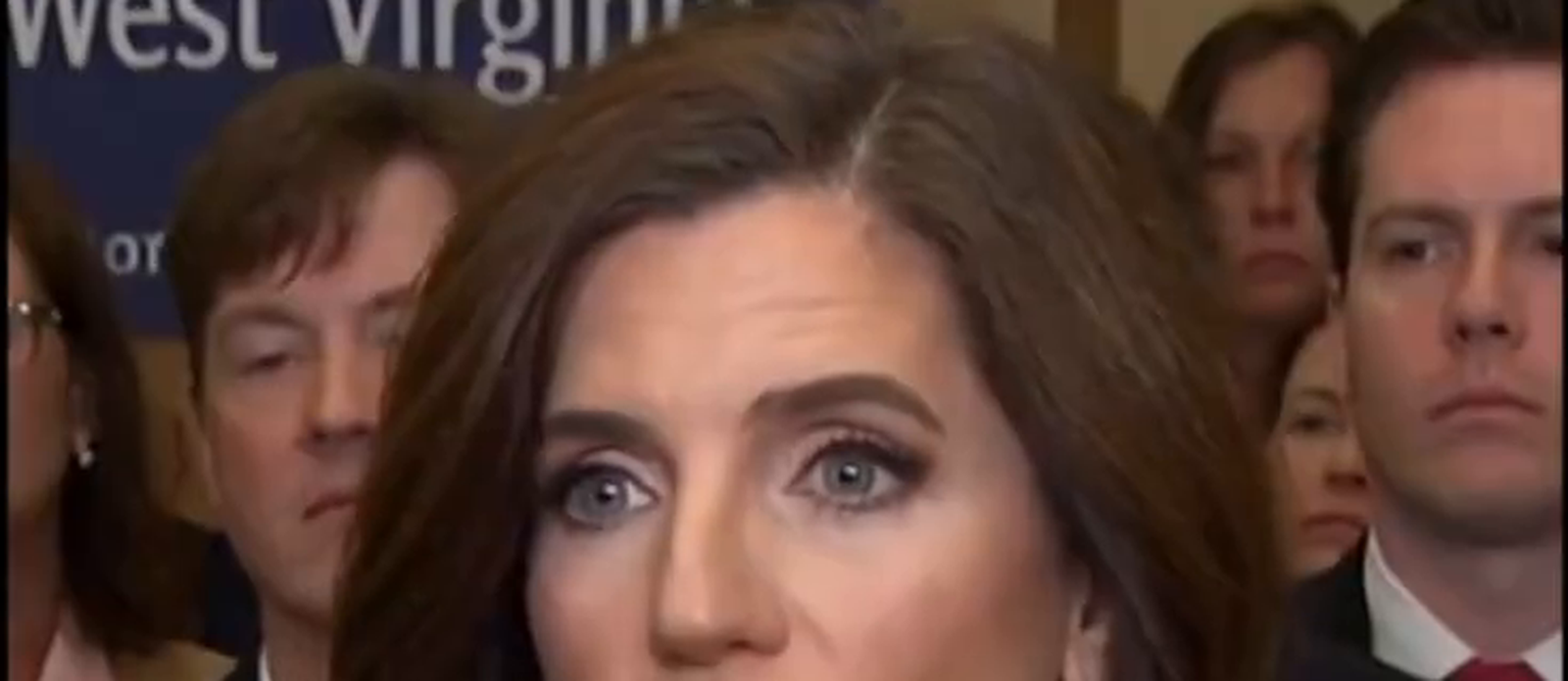 Zoomed crop of the background faces behind Nancy Mace in the press-gaggle frame, showing several onlookers with no melting, duplication, or anatomical errors on inspection