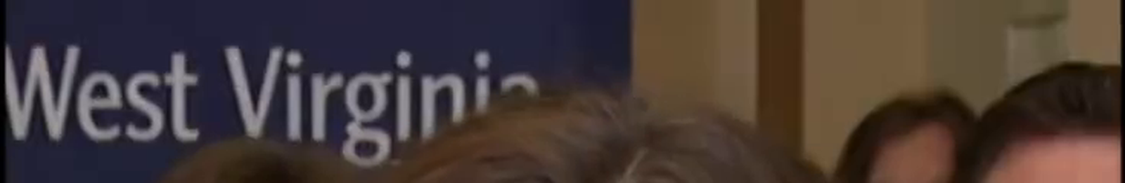 Zoomed crop of the navy 'West Virginia' banner behind Nancy Mace in the same frame, spelled correctly and cleanly rendered, in contrast to the garbled mic-flag logos elsewhere in the frame