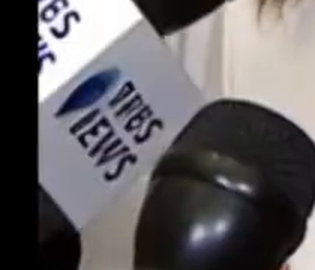 Zoomed crop of the front left microphone flag: a white flag with a blue teardrop mark and garbled italic lettering reading approximately 'PRBS' over 'IEWS,' imitating a real news wordmark